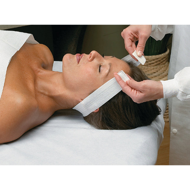 Professional esthetician performing a facial treatment using an Essenavita disposable stretch headband with Velcro closure.